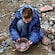 A young boy pans for gold on the rocky bank of a creek